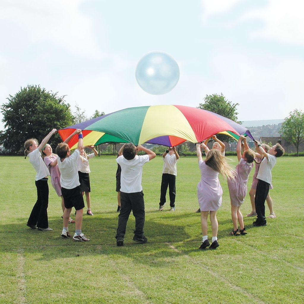 Children playing with a colourful giant parachute at a school holiday club, engaging in fun teamwork and physical activity outdoors.